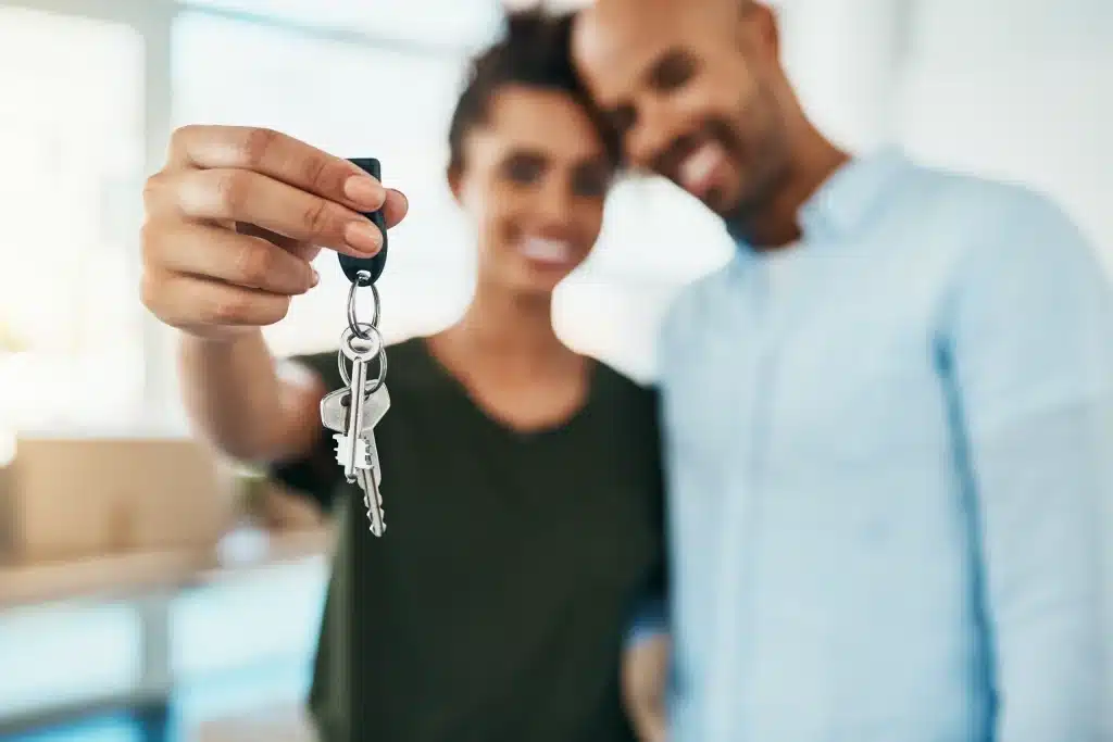 Glückliches Paar hält einen Schlüsselbund in die Kamera – symbolisches Bild für den erfolgreichen Immobilienerwerb und die Entscheidung zwischen Mieten oder Kaufen.