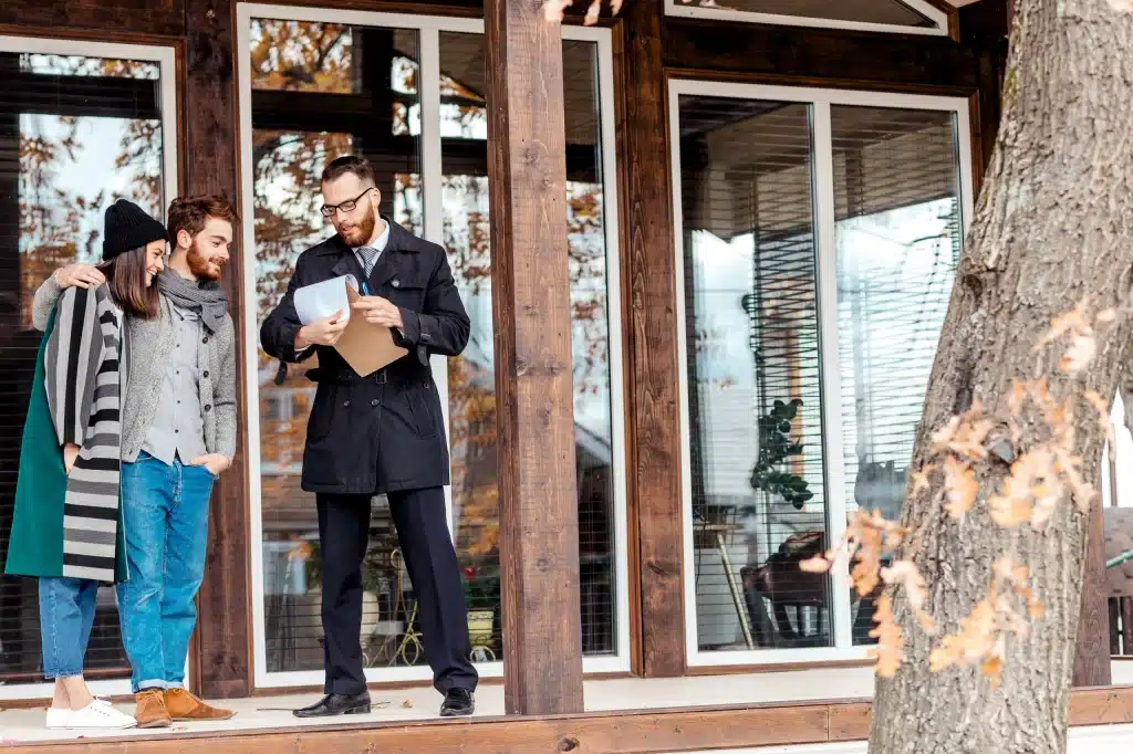Junges Paar bei einer Hausbesichtigung mit einem Immobilienmakler, der ihnen Unterlagen zeigt - symbolisches Bild zum Thema Checkliste Hausbesichtigung, um wichtige Punkte beim Immobilienkauf zu beachten.